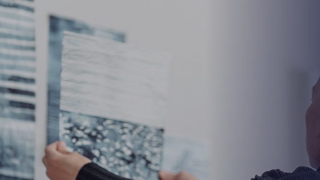 Des mains tiennent une feuille imprimée et texturée contre le mur de l’atelier