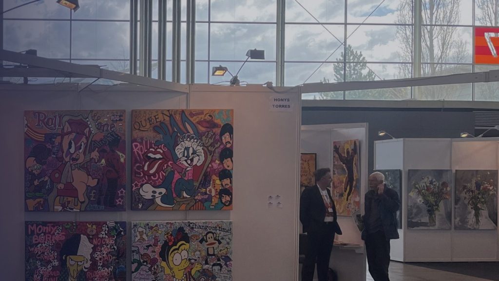 Un stand de foire d’art avec des tableaux colorés et deux visiteurs en conversation
